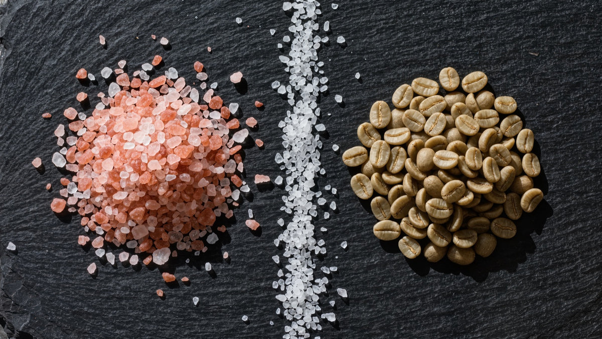 Pink Himalayan salt crystals and raw green coffee beans on dark slate